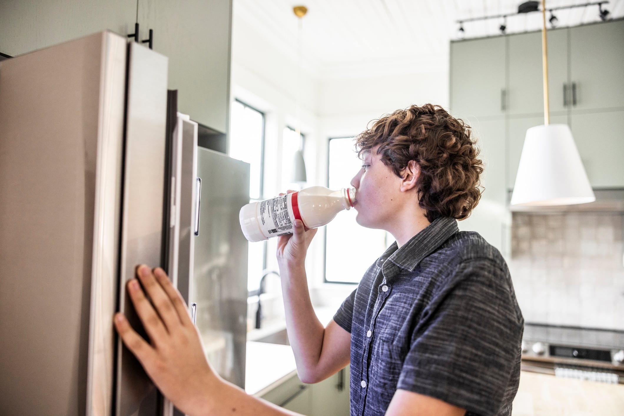 Teenage boy drinking milk from container in front of refrigerator