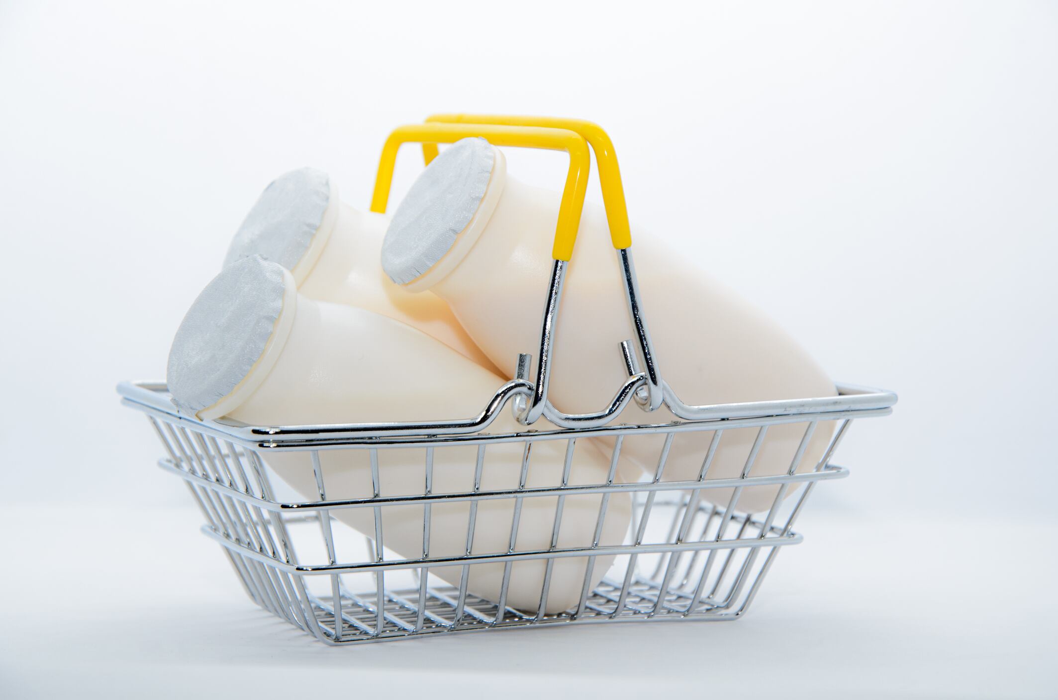 Natural yogurt with probiotics and Lactobacillus in small plastic bottles in metal shopping basket on white background. Healthy diet food, dairy products, go grocery shopping