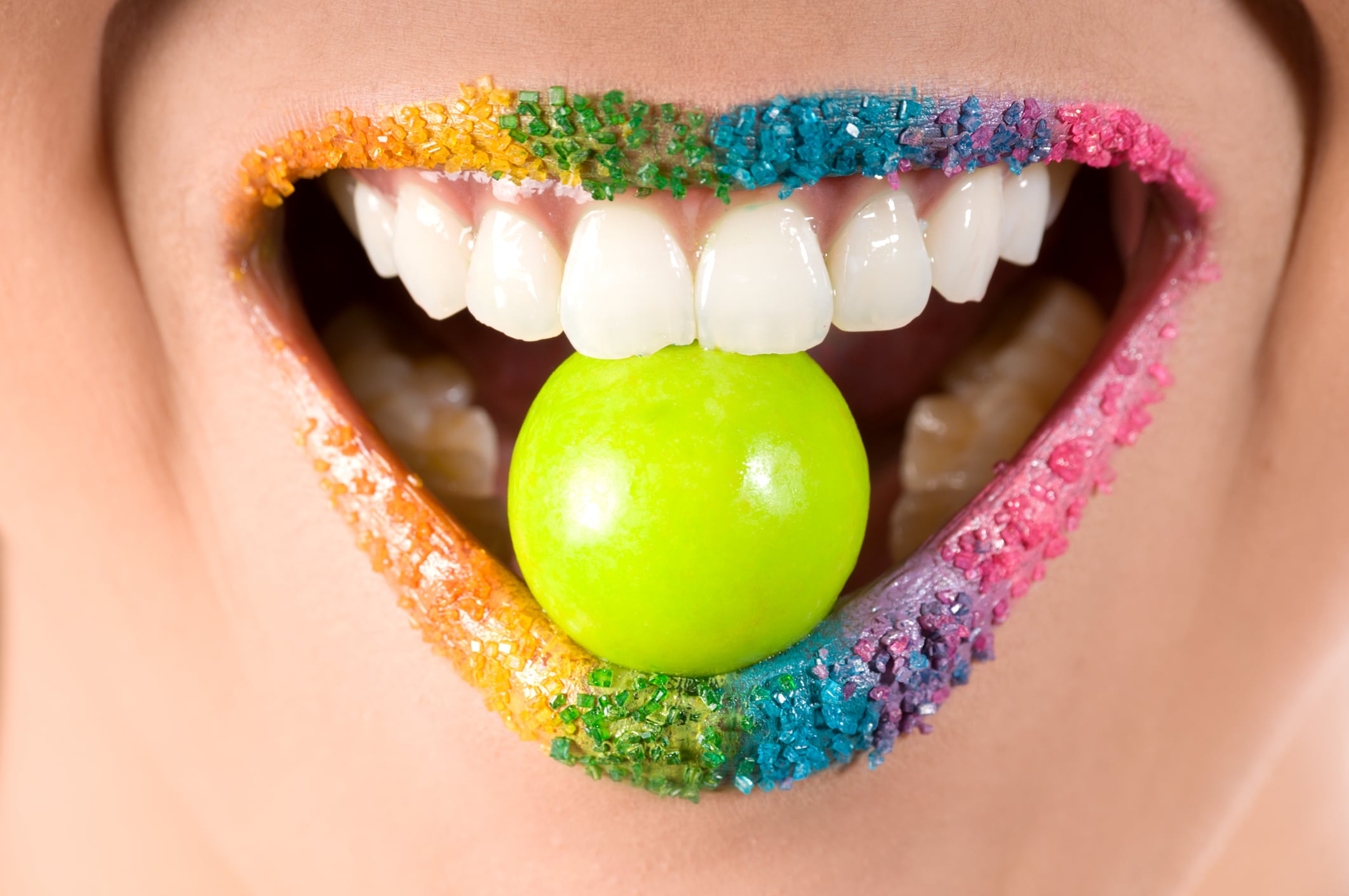 Horizontal full frame studio shot of mixed race model's smiling mouth with candy coloured striped lips and big green gumball.