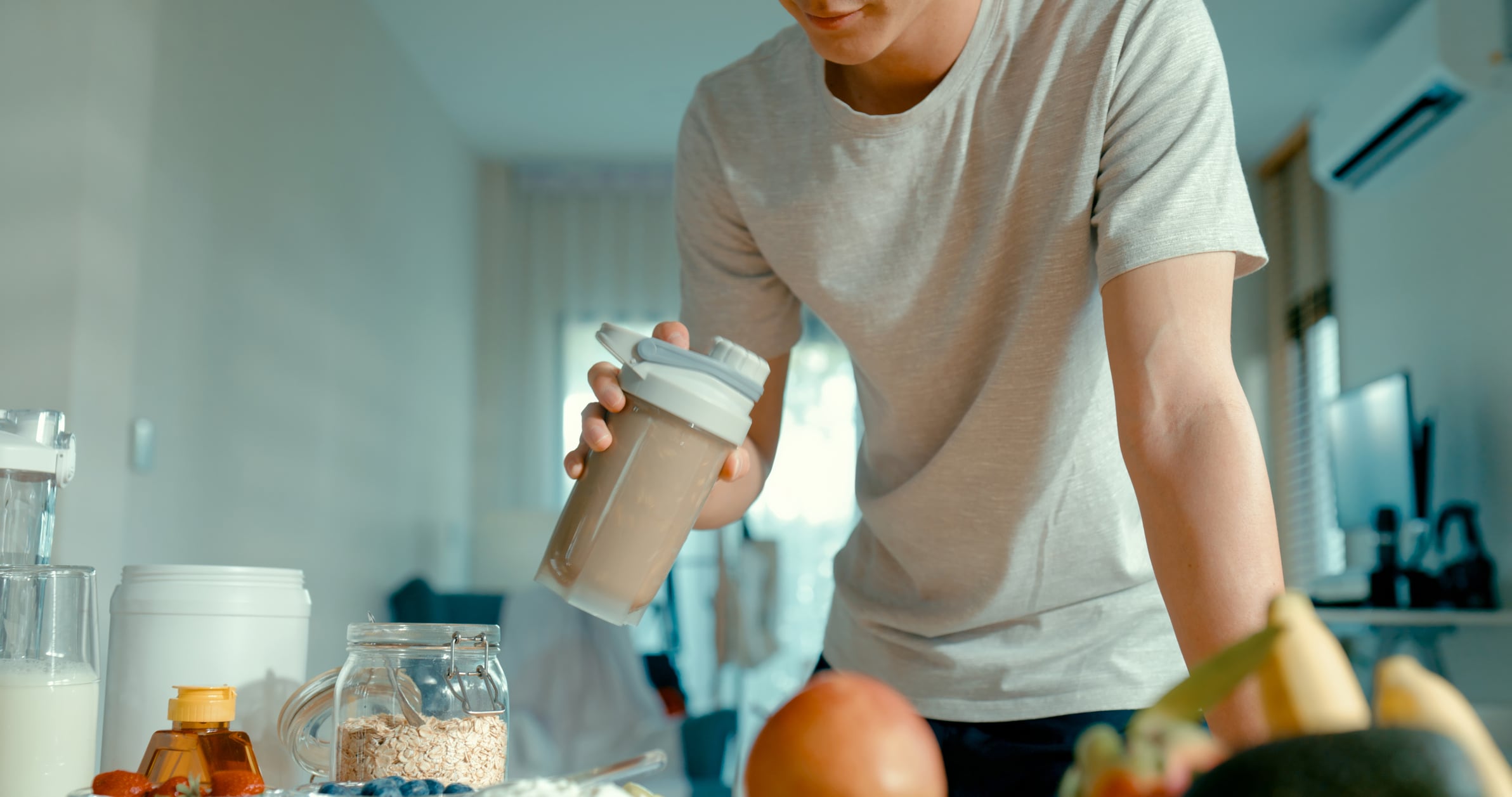 Closeup of young Asian man preparing protein shake at modern home. Diet and healthy food morning routine concept.