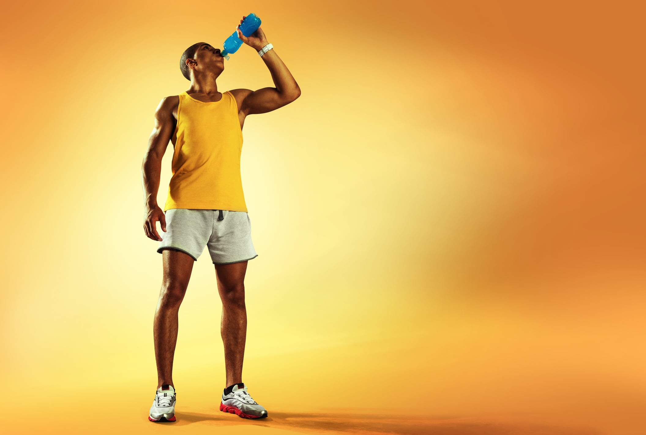 Young muscular build man drinking water of bottle after running, attractive athlete resting after workout outdoors, fitness and healthy lifestyle concept. Isolated on yellow
