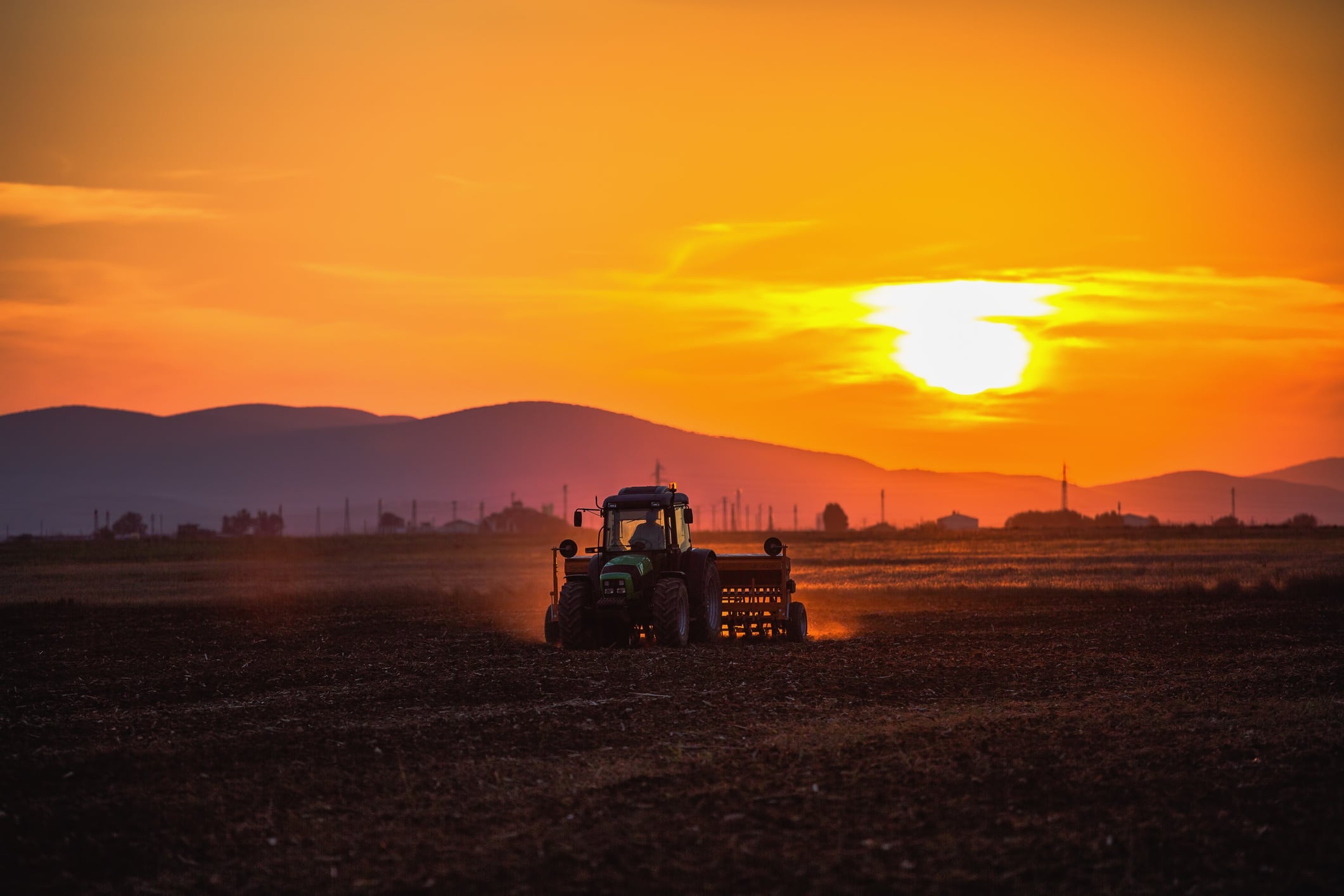 Farmer in tractor preparing land with seedbed cultivator, sunset shot.