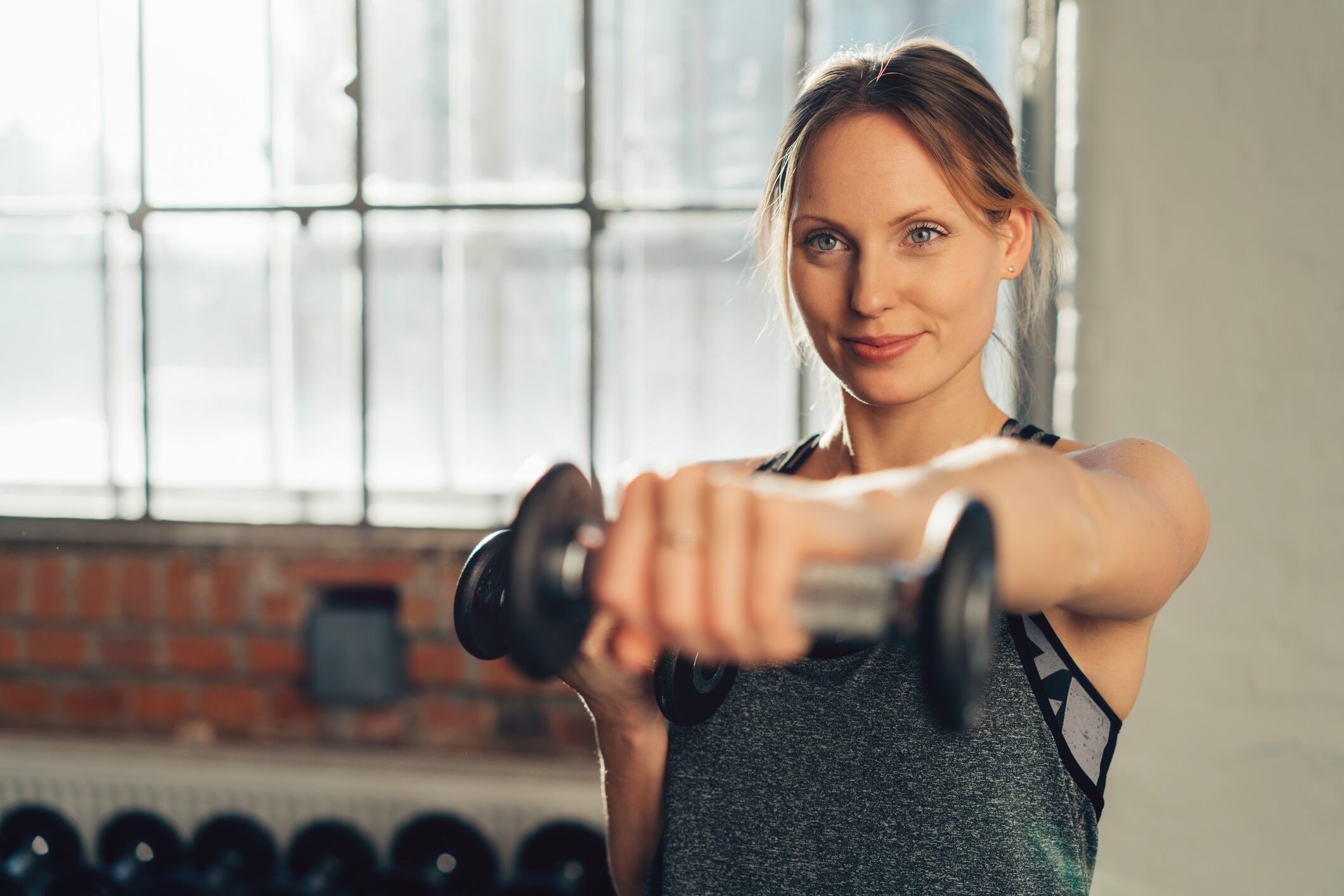 Young woman athlete training in a gym working out lifting weights with a dumbbell in her hand and copy space.