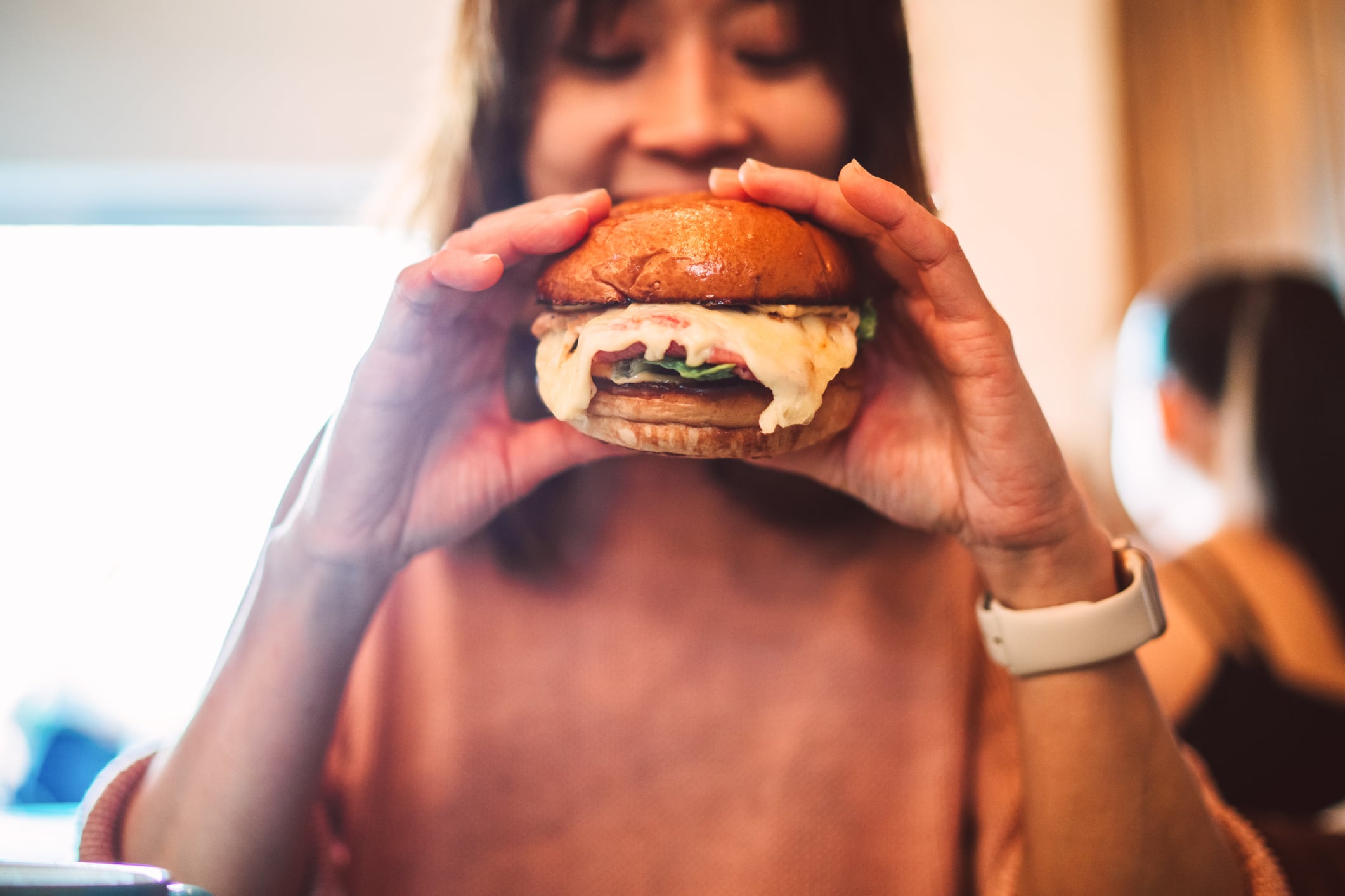 Close-up of a woman about to take a bite of a delicious, gourmet vegan burger, highlighting the indulgence and satisfaction of enjoying comfort food. Concepts of healthy eating and food indulgence.