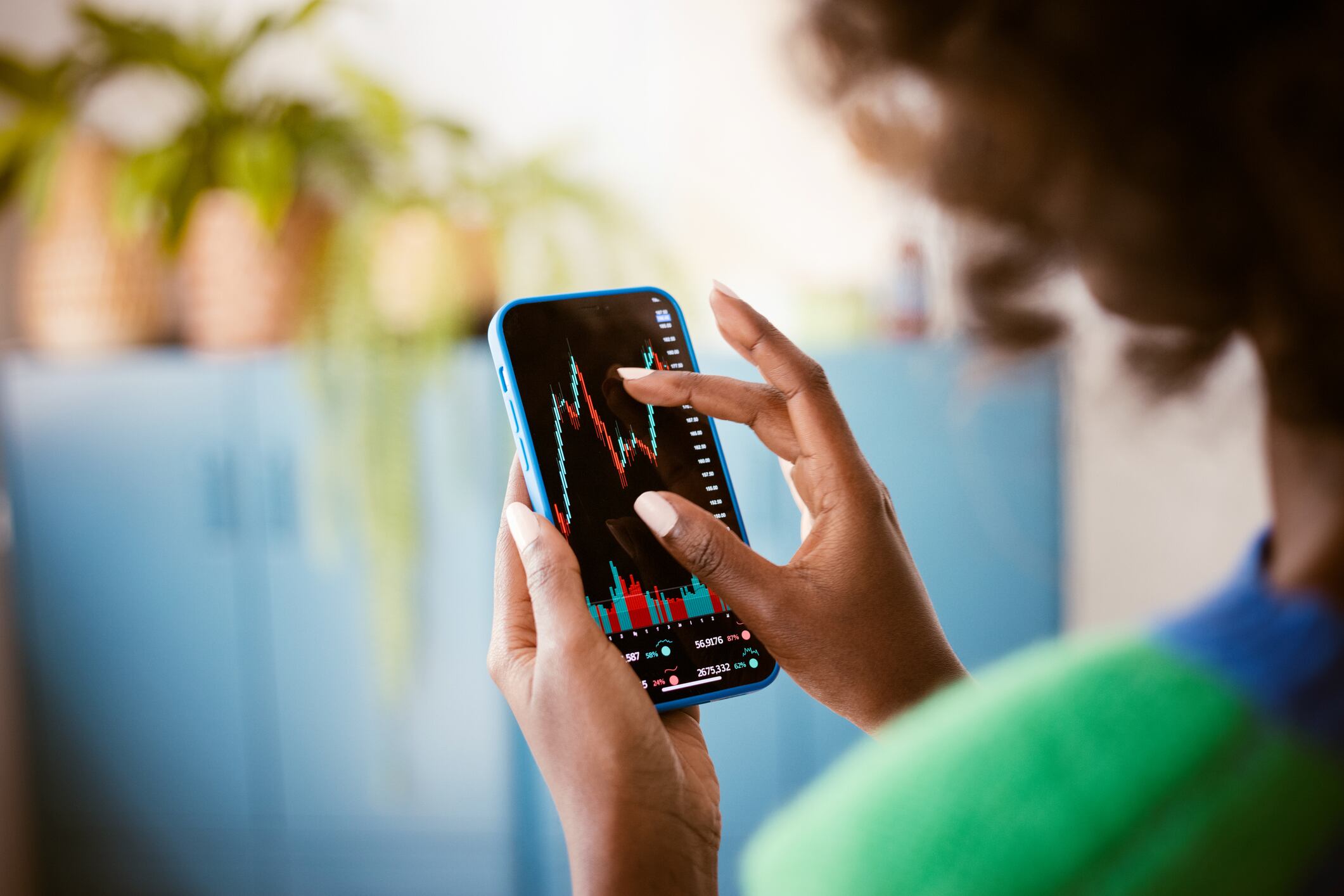 Afroamerican woman using smart phone at home, watching stock charts. Close up of hands, unrecognizable person.