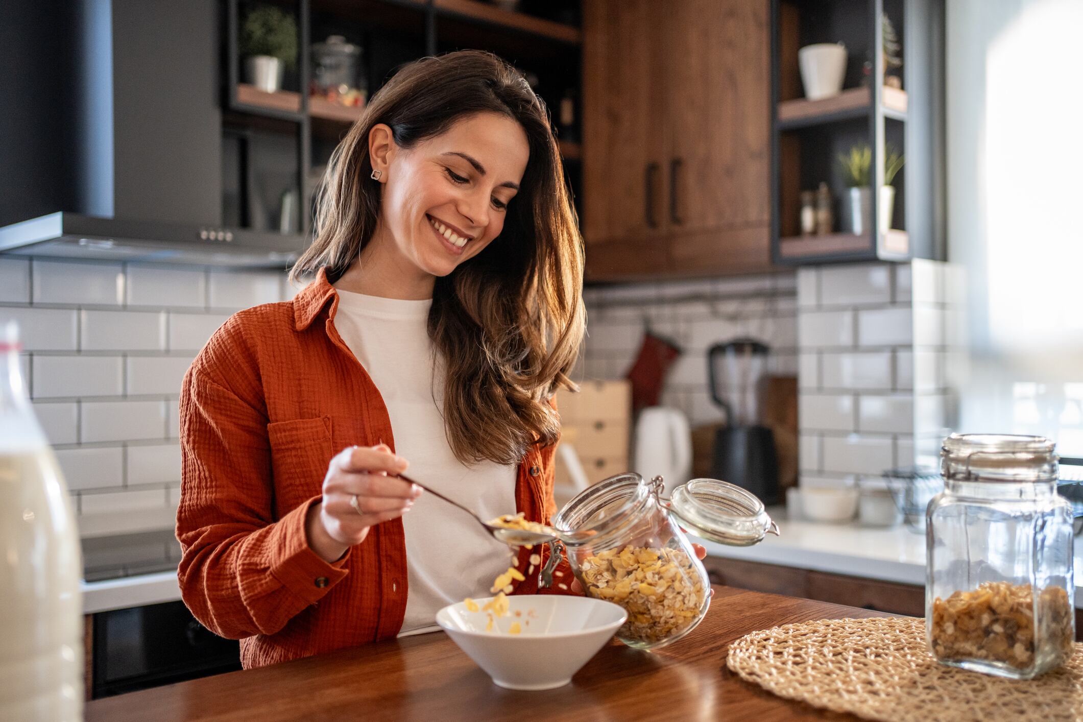 Smiling young woman pouring cereal into a bowl while enjoying breakfast in a modern kitchen, embracing a healthy lifestyle and starting the day with positivity and energy