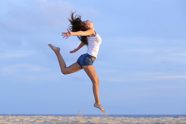 Woman jumping on the sand of the beach with the horizon in the background