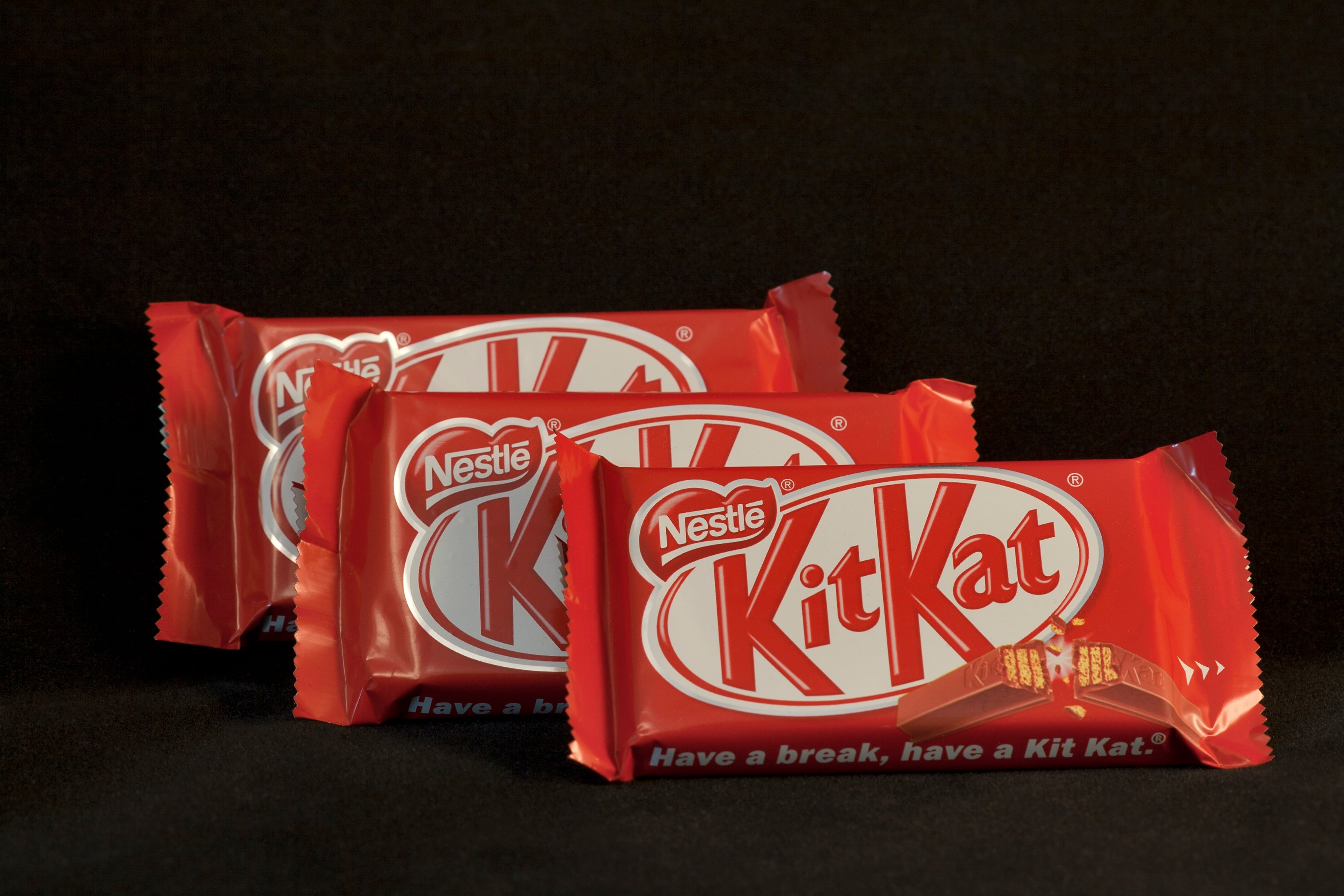 Three 4-finger KitKat Nestle chocolate bars isolated against black background.