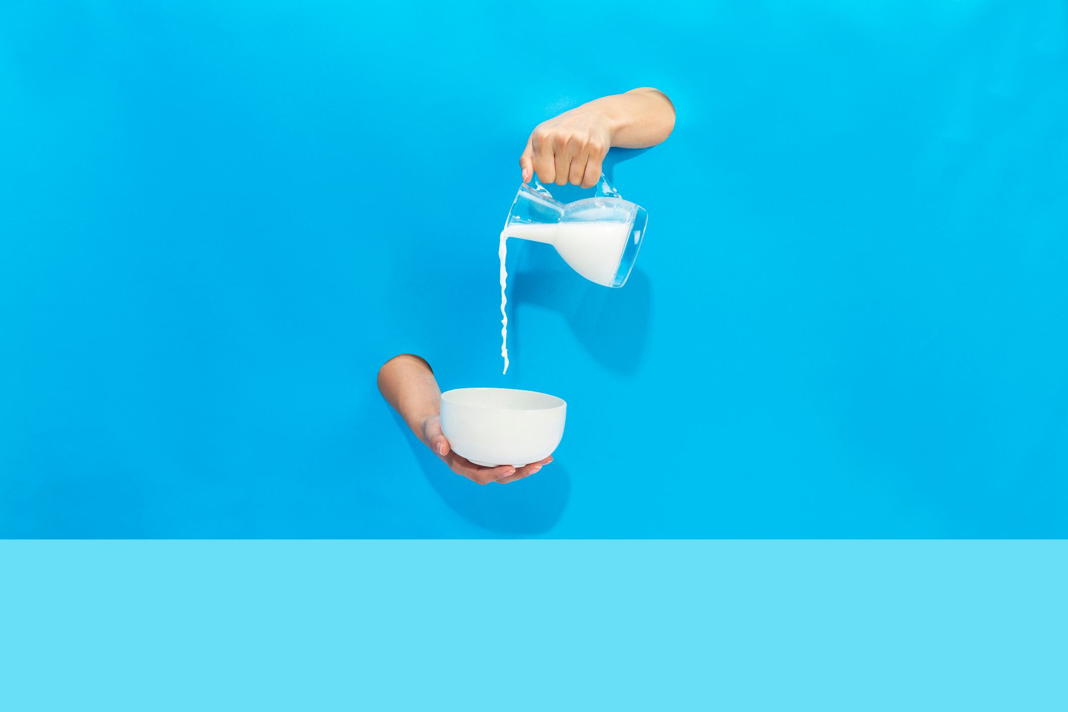 a hand pours milk from a jug into a bowl