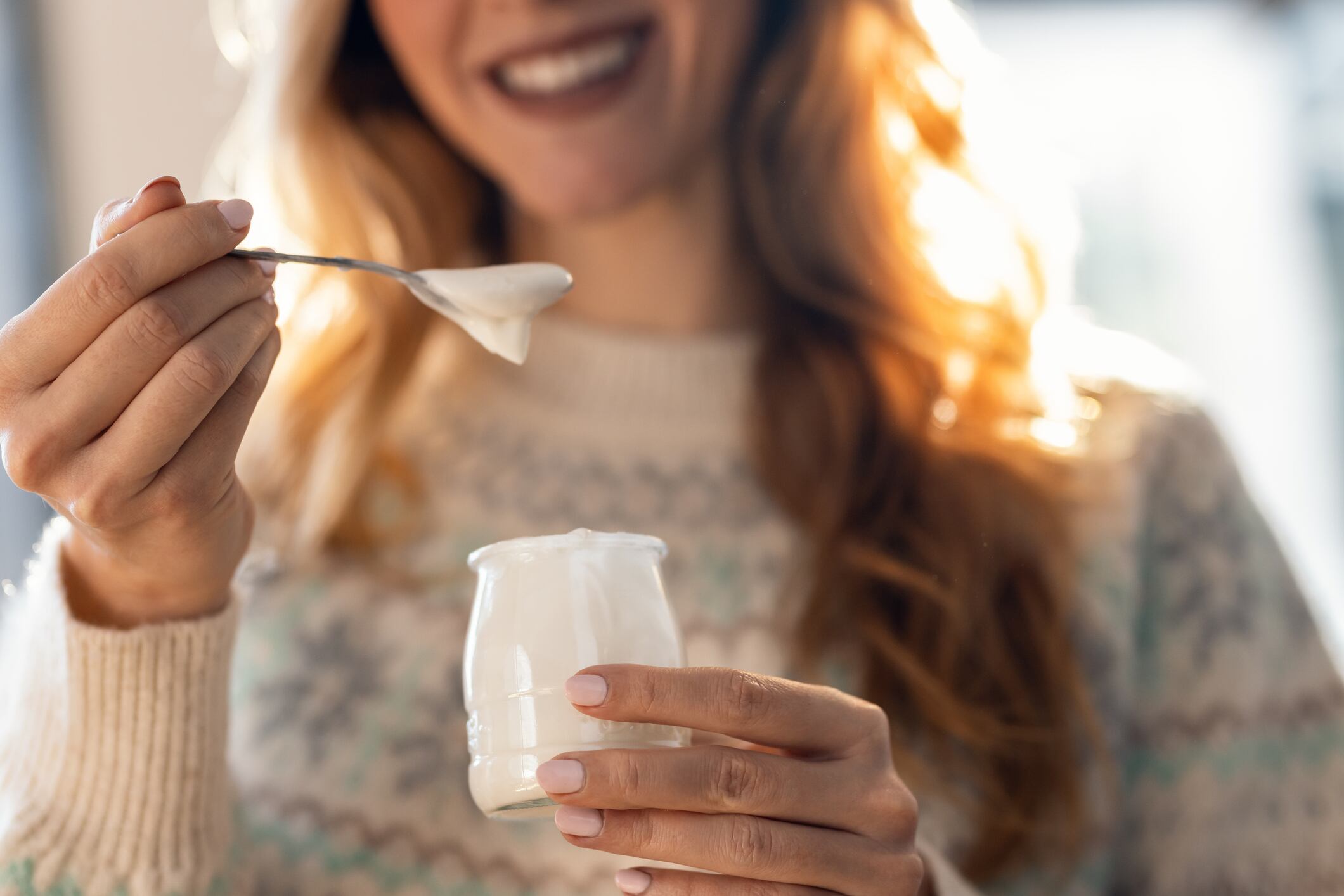Close up of happy beautiful woman eating yogurt while standing in living room at home