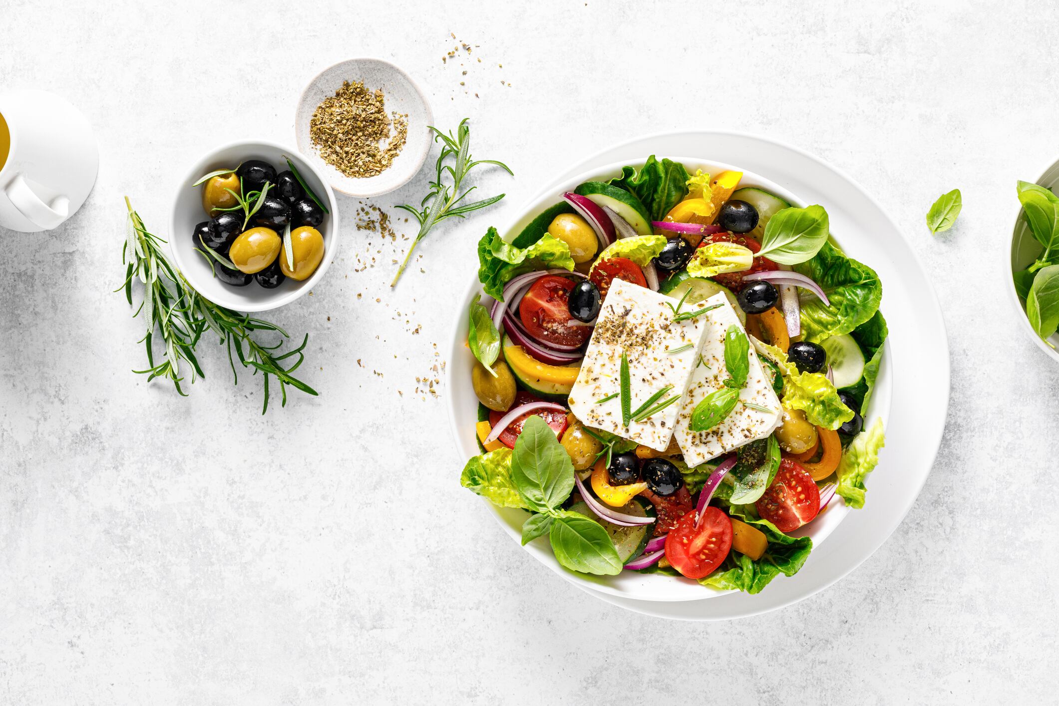 Fresh healthy vegetable Mediterranean food salad of Greek feta cheese, tomato, olives, pepper, lettuce and green basil leaves, top view