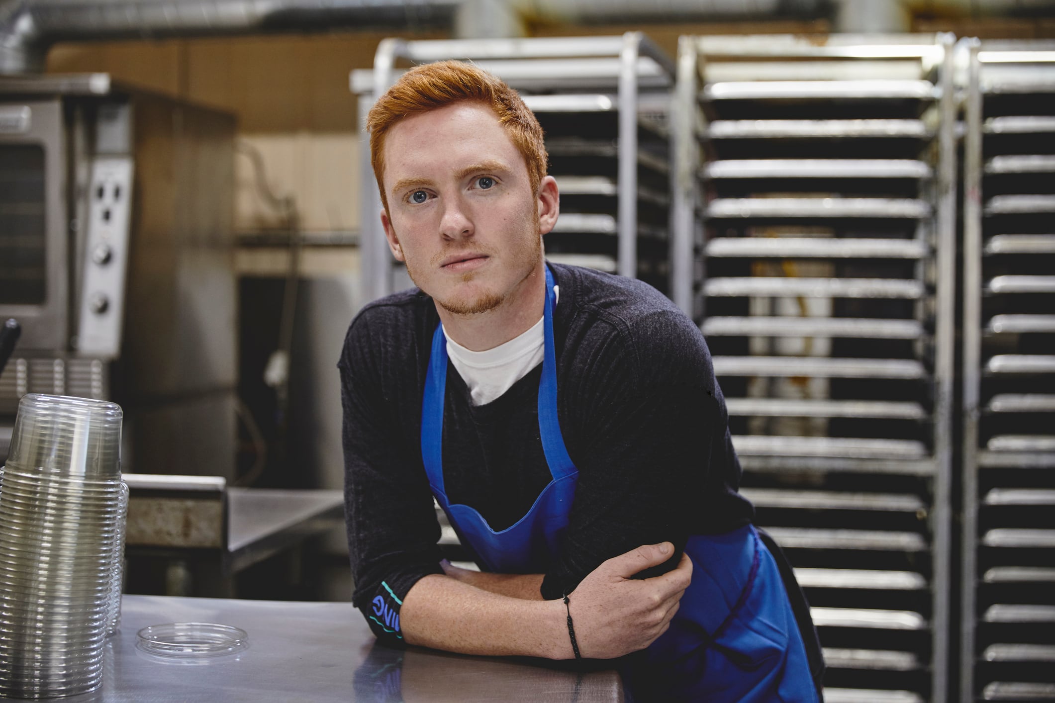 Portrait of confident male worker leaning on table against racks in nut factory