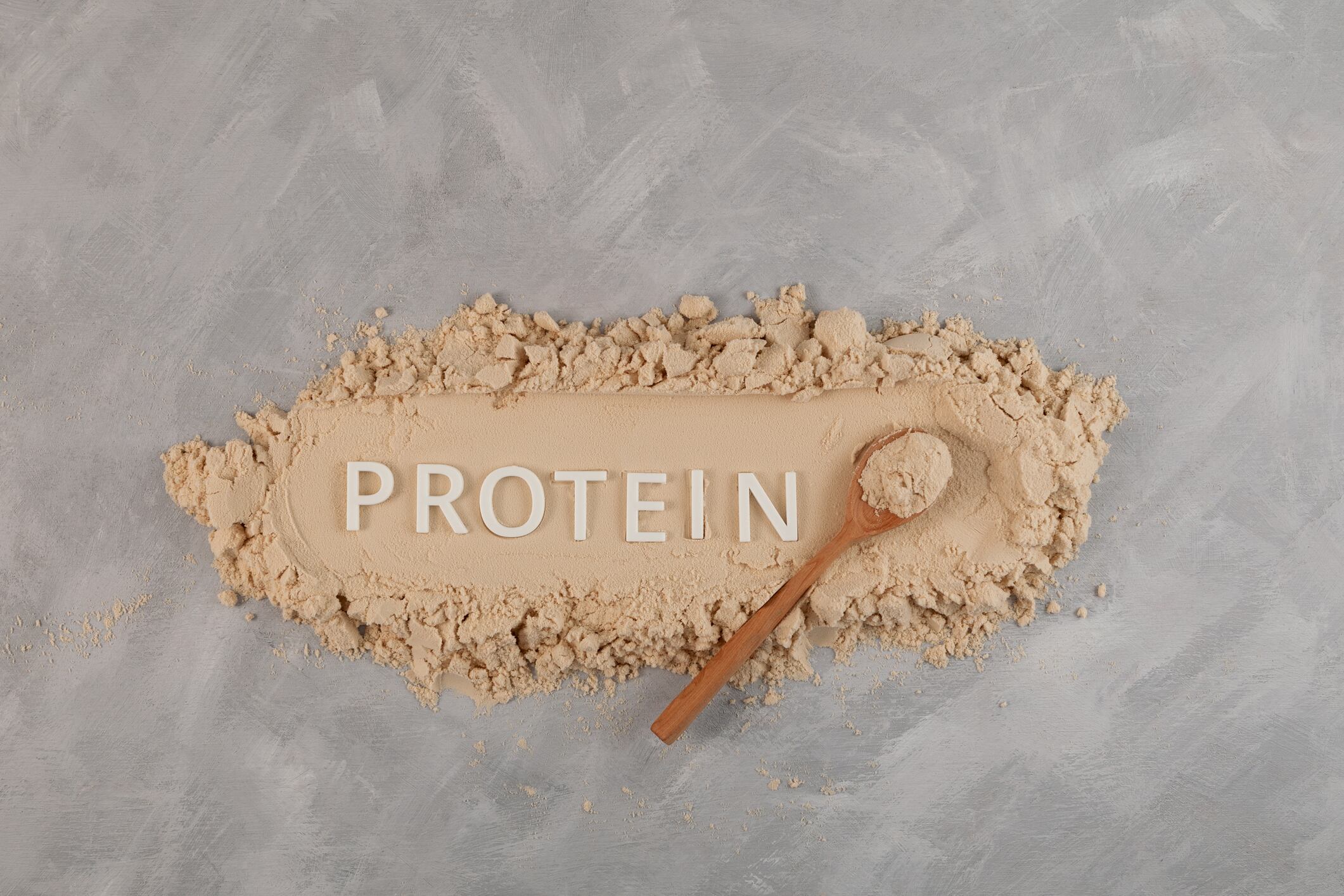 Pure Protein Powder. Food additive on grey surface. Whey Protein promotes the growth of muscle tissue, used for healthy smoothies and fitness drink. Wooden spoon and White Plastic letters.