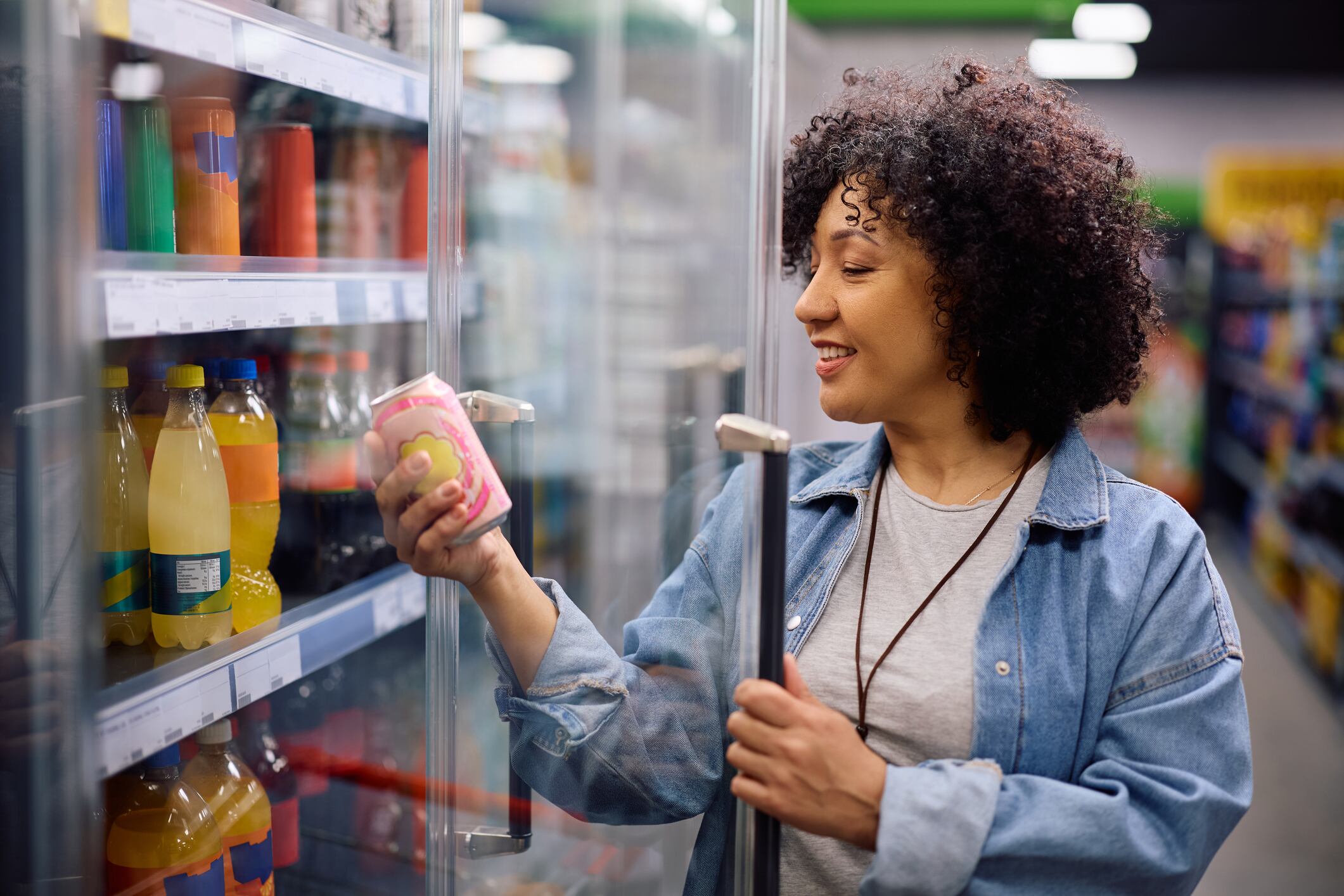 Happy mature woman buying cooled soda at the supermarket.