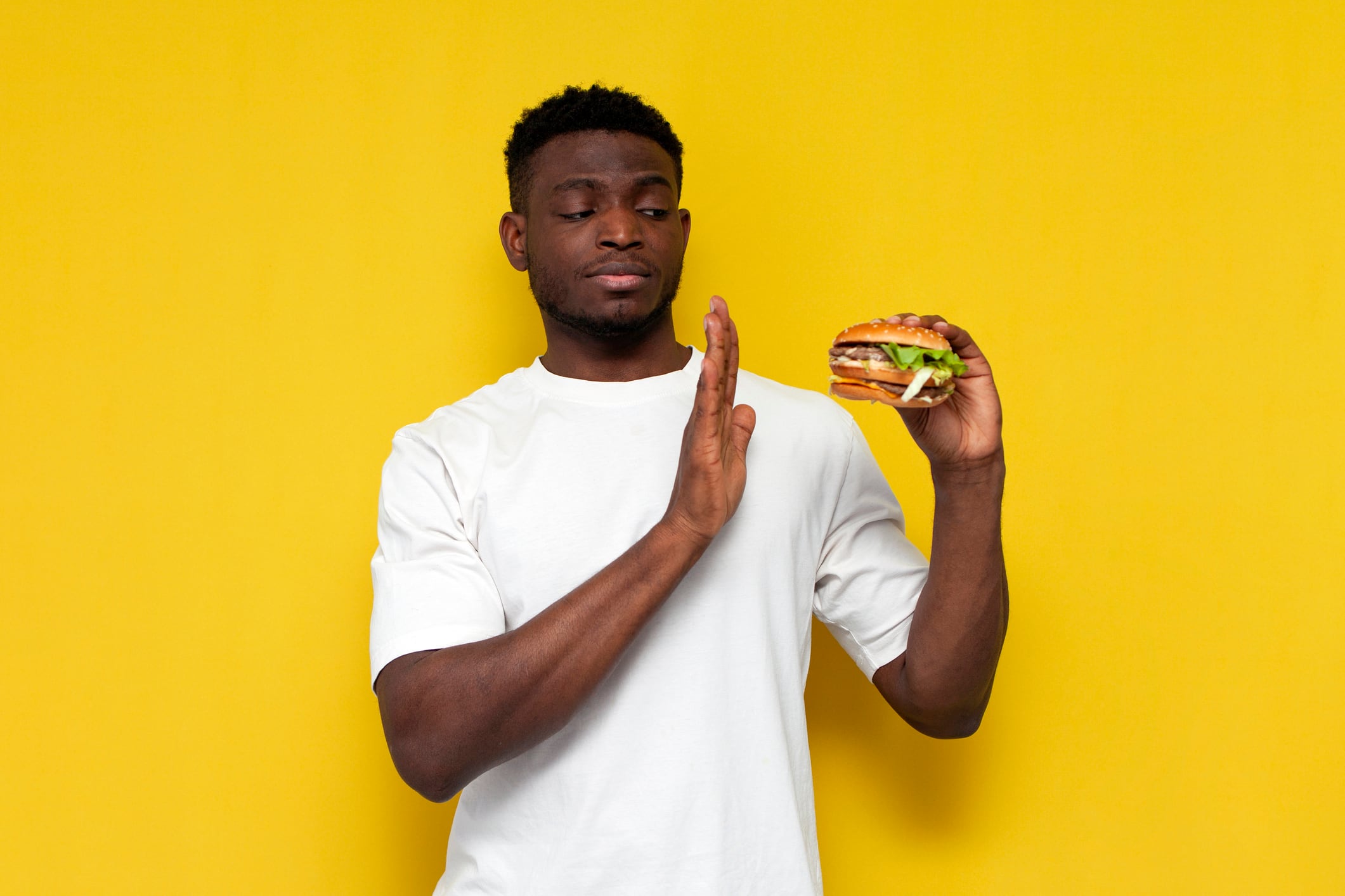 man in white t-shirt refuses burger on yellow isolated background, the guy forbids and says no to fast food