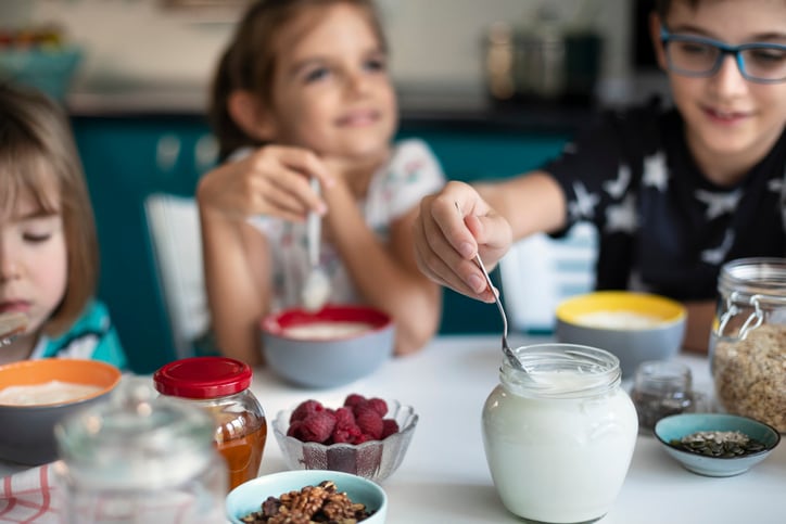 Three kids eating healthy breakfast with creamy yogurt, muesli and fresh berries.