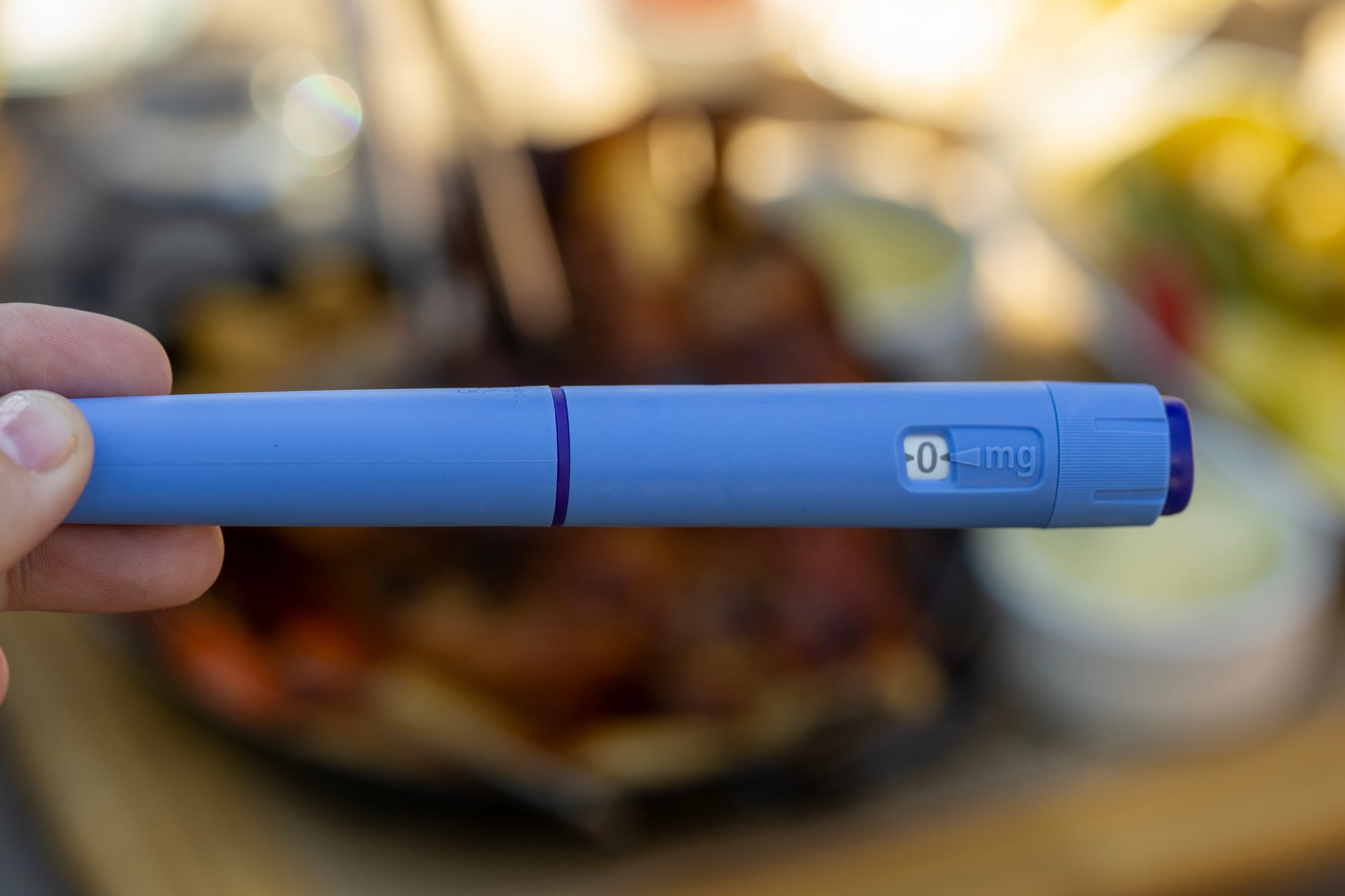 Ozempic insulin injection pen background weight loss tool blue syringe close up medical device on table next to fatty roasted pork knuckle food concept of medicine healthcare diabetes.