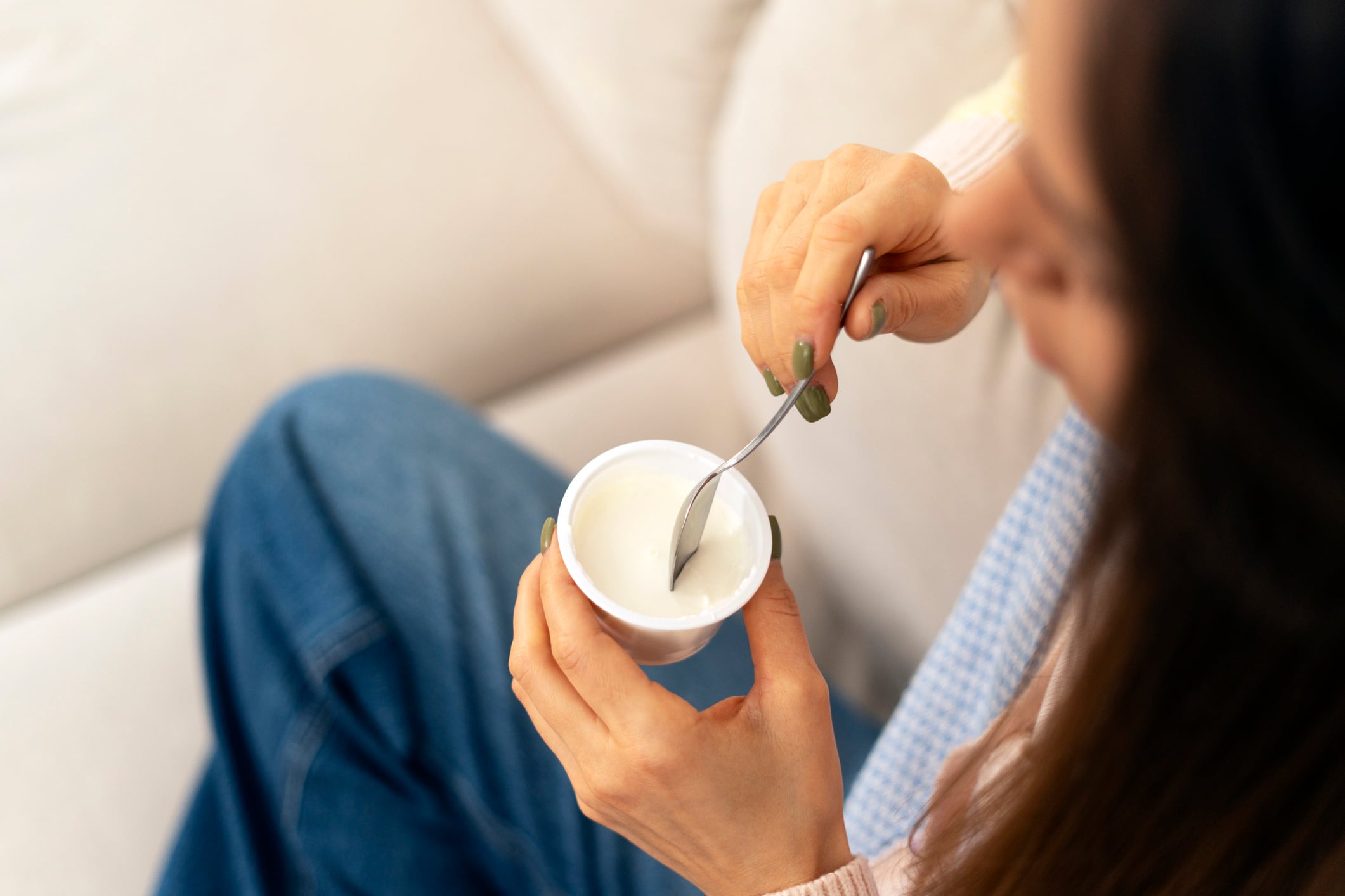 Woman enjoying a creamy yogurt snack on the sofa, savoring a delicious and nutritious treat while embracing a healthy lifestyle and prioritizing wellness at home