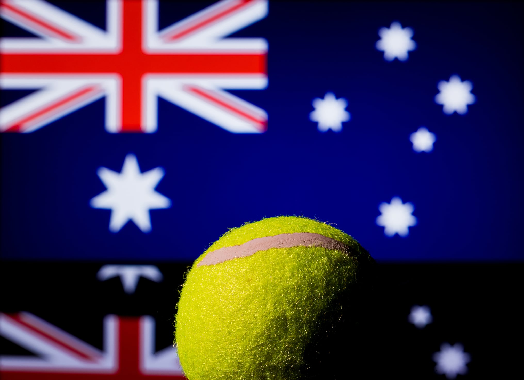 Yellow Tennis Ball on black mirror with Australian Flag in the background out of focus