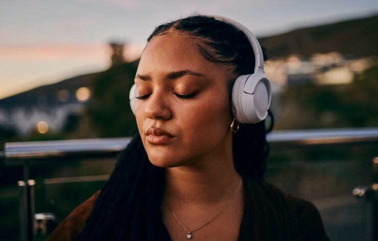 A serene young woman with braided hair and headphones enjoys music outdoors during sunset, capturing a moment of calm and introspection.